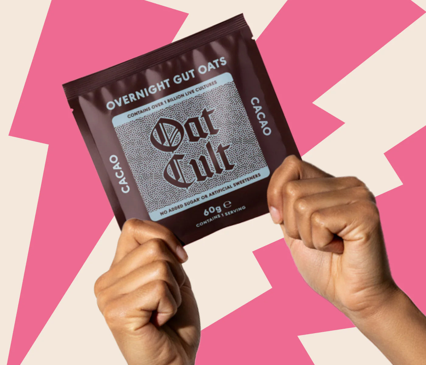 Hand holding a package of 'Oat Cult' overnight gut oats against a pink and beige geometric pattern background.